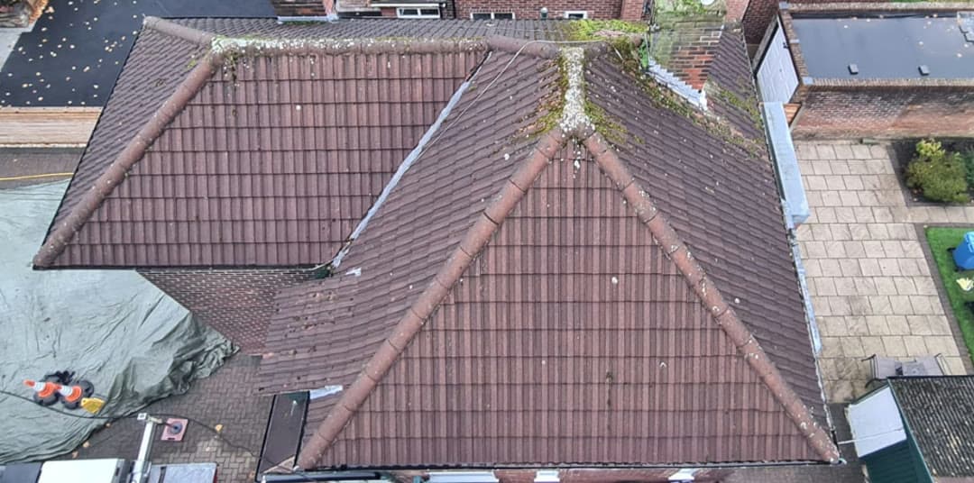 A hip roof from above, dark brown with moss along every ridge